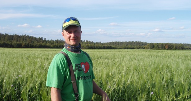 Bonde Ola Johansen, iført en gul caps og en grønn t-skjorte med teksten "Æ <3 landsbruk", står foran gress klart for høsting.