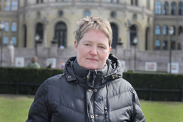 Kvinne i svart boblejakke ser alvorlig mot kameraet. Hun står foran Stortinget i Norge.